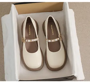Top view of cream Mary Jane shoes with pearl strap details inside a black shoebox
