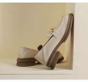 Close-up of beige platform loafers with a gold metal buckle and chunky brown sole