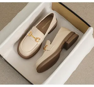 Detail view of beige platform loafers with gold buckles inside a premium shoebox