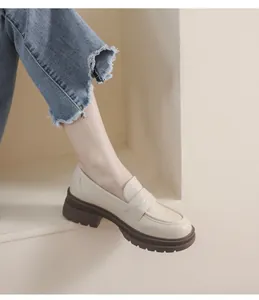 Detalle de mocasines de plataforma crema con suela marrón gruesa y vaqueros deshilachados