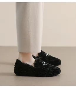 Detail of black faux fur loafers with a white bow on smooth beige trousers background