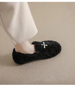 Close-up of black fuzzy loafers with white cross metal buckle on a cozy beige carpet