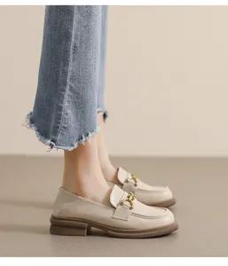 Détail de mocassins en cuir beige avec chaîne dorée portés avec un jean bleu