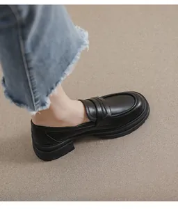 Vista lateral de mocasines de plataforma en cuero negro mate con vaqueros deshilachados