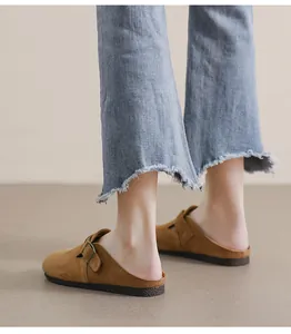 Dettaglio di sabot in camoscio marrone con fibbia metallica e jeans in denim