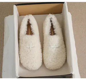 Close-up of white plush loafers with star buckle and soft faux fur texture in a gift box