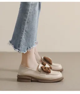 Detalle de mocasines de cuero beige con lazo marrón y hebilla de metal dorada