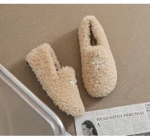 Detailed top view of beige faux fur loafers featuring white cross-stitch embroidery details