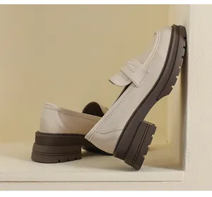 Detalle de mocasines de cuero beige con suela gruesa de goma marrón y correa clásica