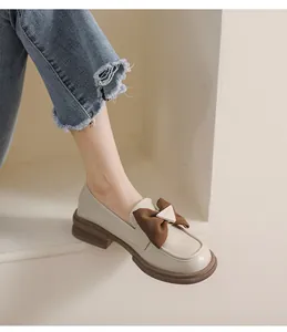 Detalle de mocasines crema con lazo marrón y hebilla metálica sobre cuero suave