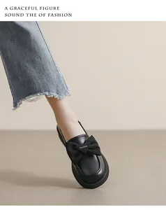 Detalle de mocasines de cuero negro con un lazo grande y un logo de metal triangular