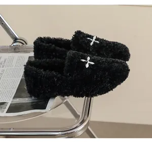 Detail of black plush loafers with white flower charms on a clear designer chair
