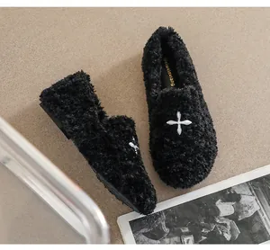 Top view of black faux fur loafers with silver cross charm on beige background