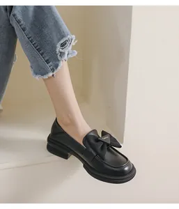 Detalle de mocasines negros con lazo y placa metálica sobre cuero mate de calidad