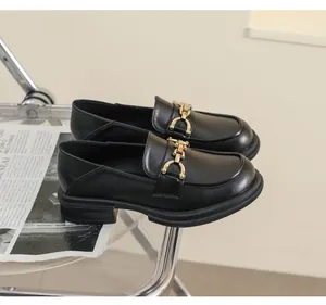 Détail de mocassins noirs avec boucle chaîne dorée sur fond de mode minimaliste