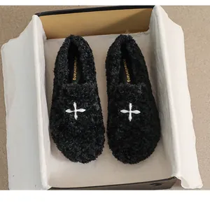Detailed top view of black fleece loafers with silver metal cross in a branded shoebox