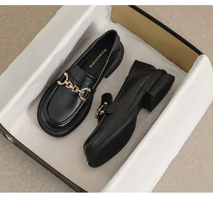 Détail de mocassins en cuir noir mat avec chaîne dorée et talon bloc épais