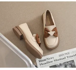 Detalle de mocasín beige con lazo marrón y hebilla metálica triangular decorativa