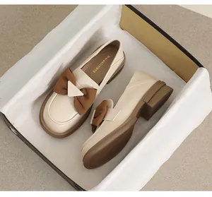 Detalle de un mocasín crema con lazo marrón y hebilla metálica en caja de zapatos