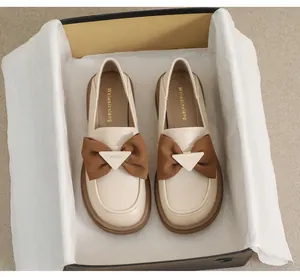 Detalle de mocasines beige con lazo marrón y hebilla de metal con el texto Fashion grabado