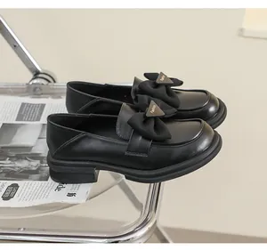 Detalle de mocasín de cuero negro mate con lazo de tela y emblema Fashion metálico