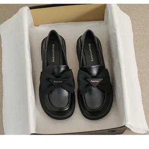 Detalle de mocasín retro negro con lazo de tela y hebilla metálica dorada Fashion en caja