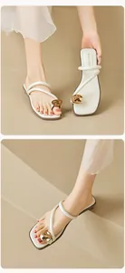 Gros plan de sandales à bout boucle blanc cassé avec sphère dorée et brides fines