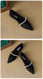Detailed view of black pointed-toe flat shoes with a decorative pearl strap across the vamp