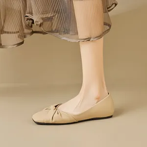 Elegant beige flat shoes for women with round toe and twisted knot detail on grey background