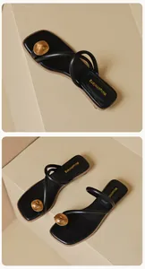 Détail de sandales noires à entredoigt avec grande pièce en métal doré et bout carré