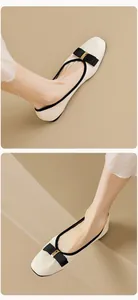 Detail von cremefarbenen flachen Ballerinas mit schwarzer Schleife und Goldschnalle