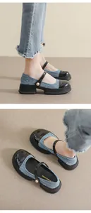 Detail van denim Mary Jane schoenen met zwarte lakneus en witte parelmoeren gespdecoratie