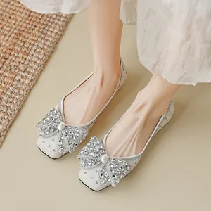 Glinsterende zilveren platte schoenen met strass-strik gedragen door een model