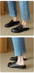 Close-up of black leather penny loafer mules with detailed stitching on light brown rug