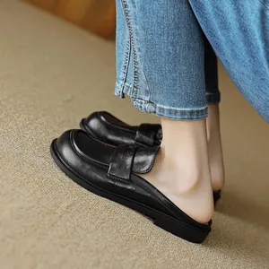 Classic black leather round-toe mule loafers worn with jeans on a textured carpet