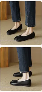 Detail view of black leather round-toe flat shoes with pleated design on beige woven rug