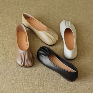 Flat round-toe pleated loafers in black, beige, and tan displayed on textured fabric