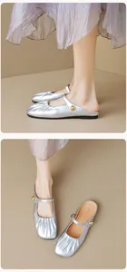 Macro shot of silver pointed-toe mule shoes with metallic finish and gold ball buckle strap