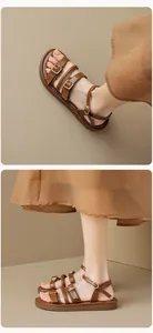 Detalle de sandalias planas de cuero marrón con hebillas de metal dorado y diseño de tiras
