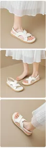 Detail view of white cross-strap sandals with soft brown soles worn with a pleated skirt