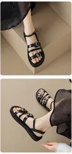 Detalle de sandalias negras con correas, hebillas doradas y costuras blancas en contraste