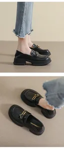 Detail of black platform loafers featuring a golden heart buckle and thick sole