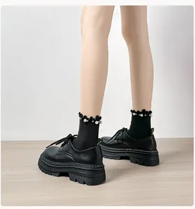 Detalle de zapatos derby negros con plataforma, costuras blancas y calcetines con perlas