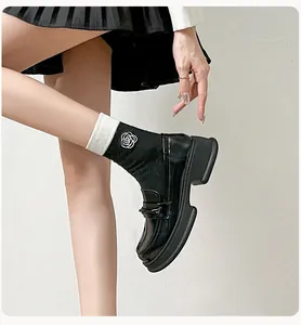 Close-up of black glossy platform loafers featuring white trim socks and rose embroidery