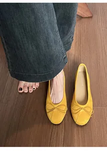 Détail de ballerines jaunes en daim avec nœud sur un sol en bois marron