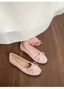 Detail van zachte roze suède ballerina's met een strikje op een houten vloer