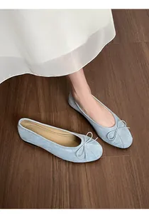 Gros plan de ballerines en daim bleu clair avec nœud sur un sol en bois sombre