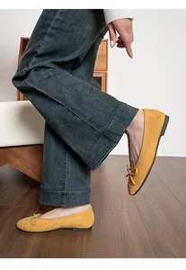 Detailopname van gele imitatiesuède ballerina's met een strikje op houten vloer