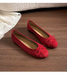 Gros plan de ballerines en daim rouge avec nœud sur un sol en bois foncé