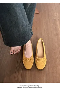 Detail van mosterdgele suède ballerina's met strikdecoratie op houten vloer